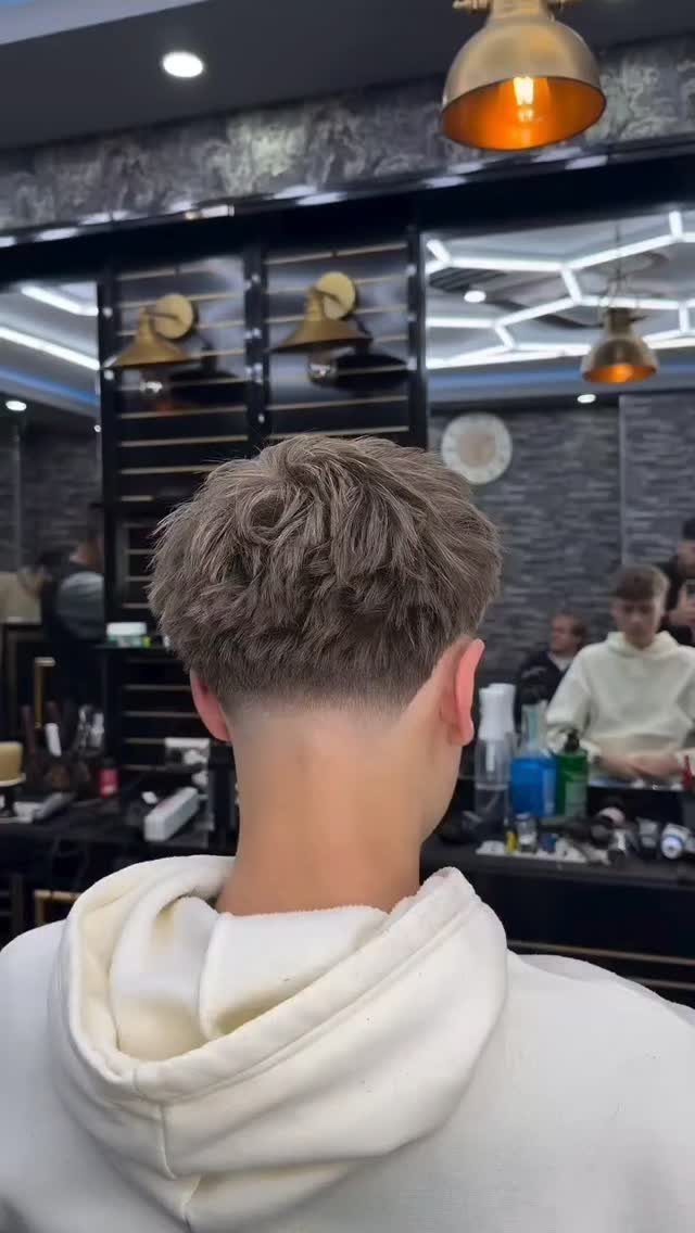 Man with a drop fade haircut and textured top in a barbershop setting.