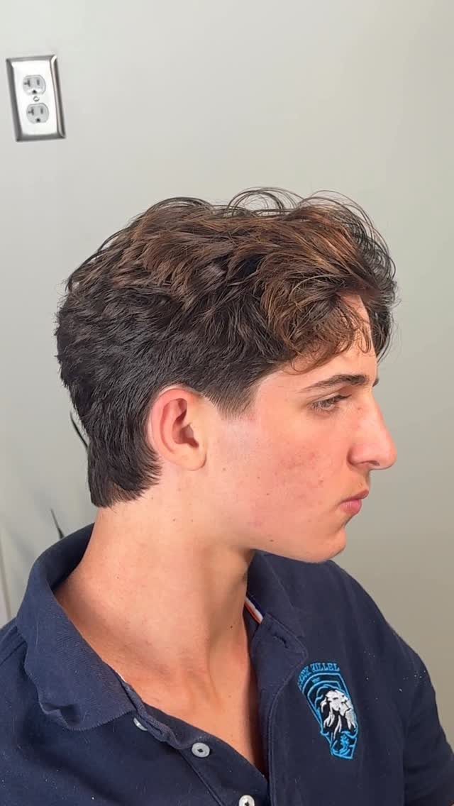 Young man with voluminous wavy brown hair and a clean taper fade haircut.