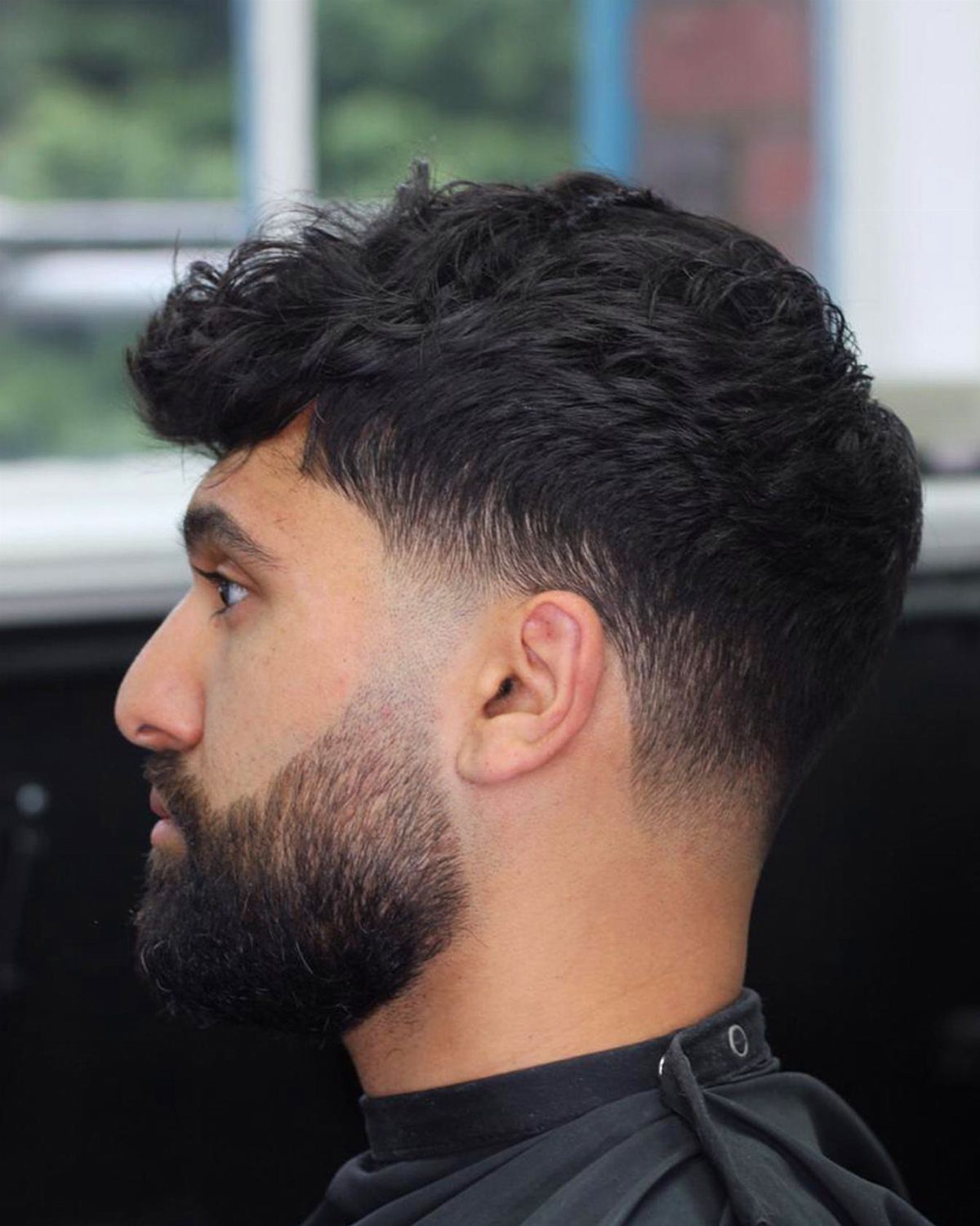 Man with wavy hair, low taper fade, and a groomed beard fade.