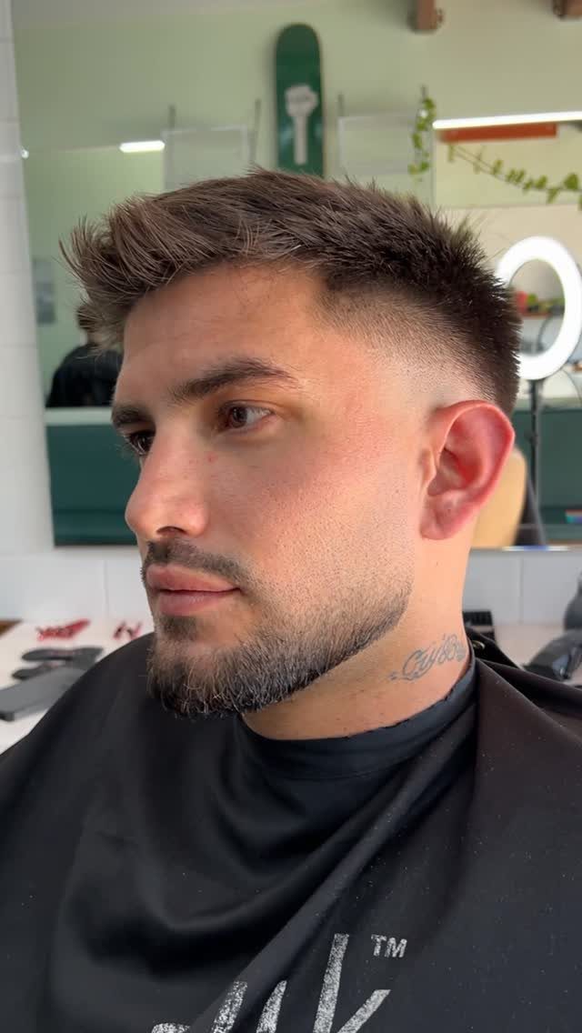 Man with a low taper fade haircut and groomed beard in a barbershop.