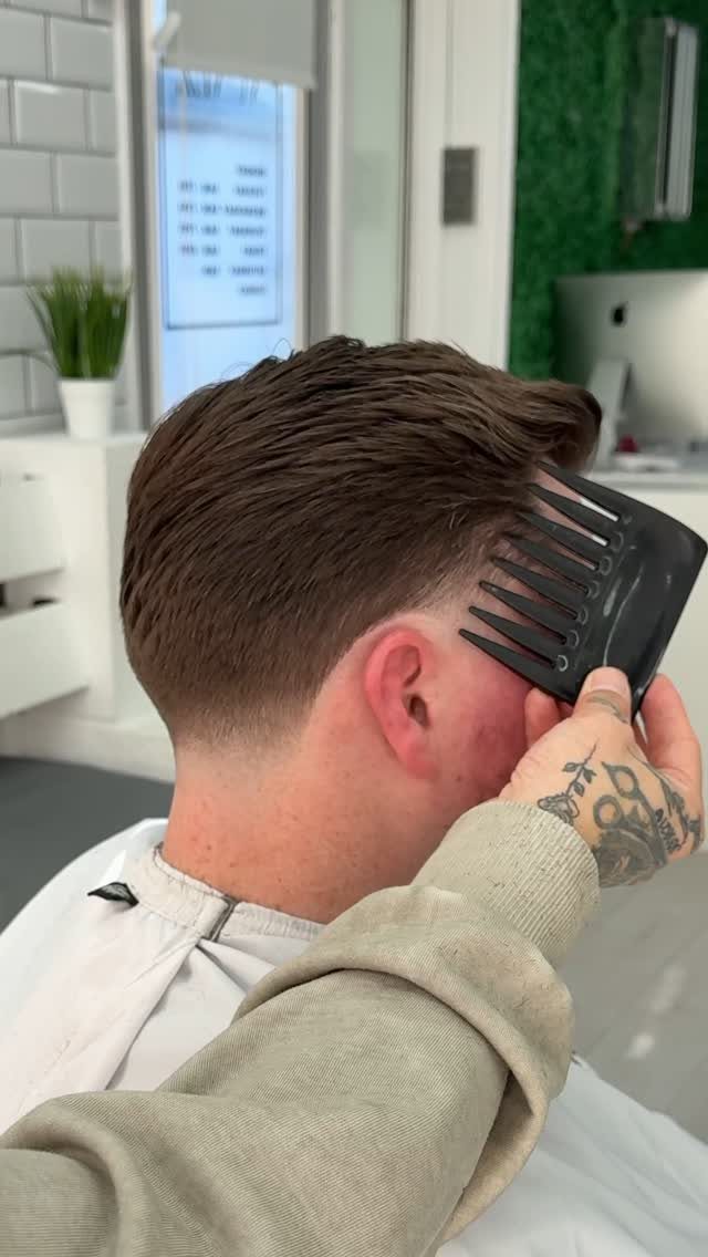 Man receiving a low taper fade haircut with brown hair being combed.