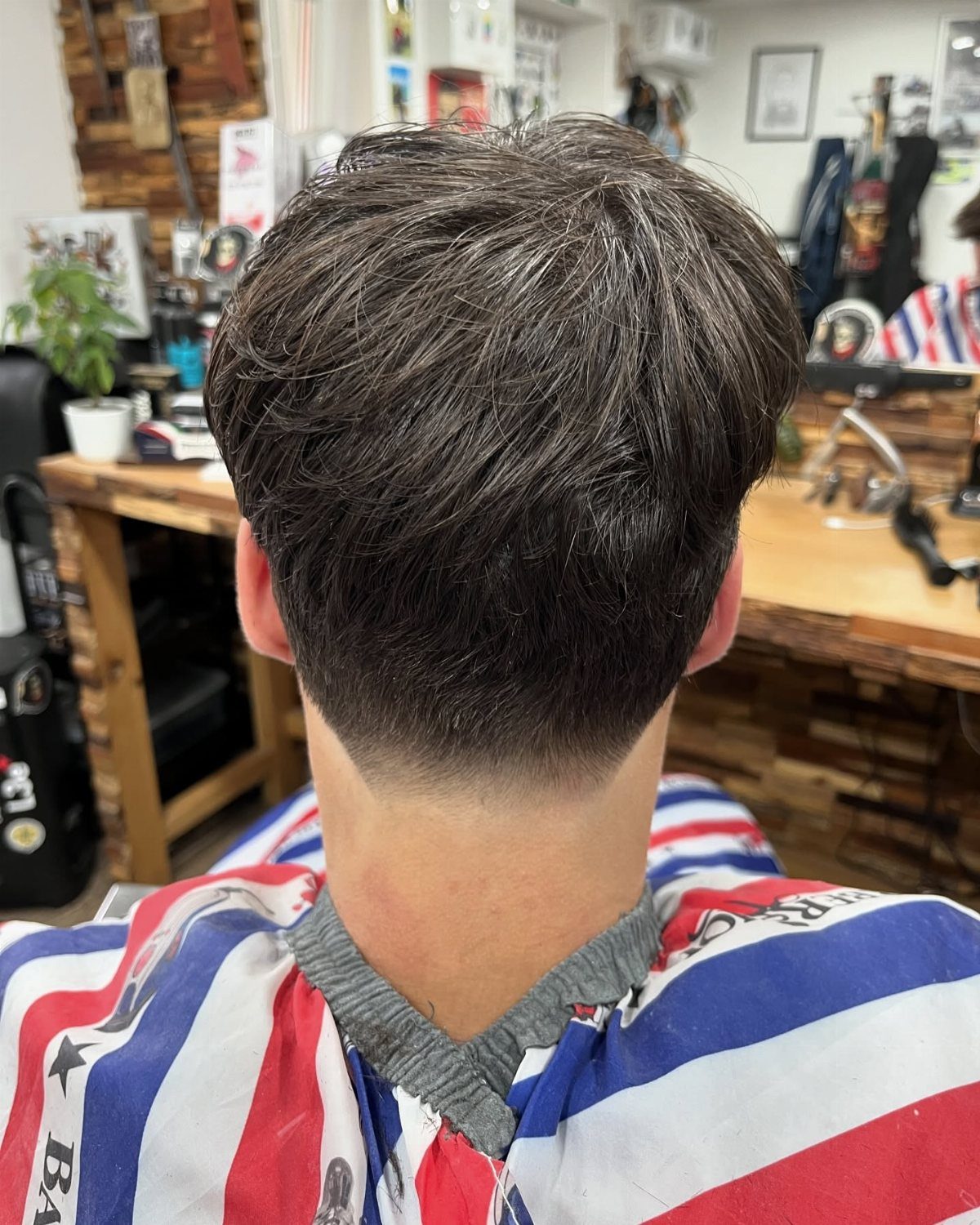 Back view of a brown hair low taper fade haircut in a barbershop.