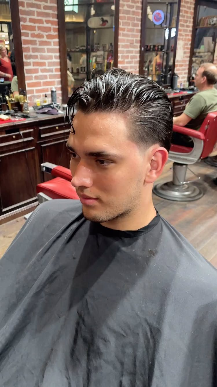 Man with dark hair styled in a glossy slick back at a barbershop.