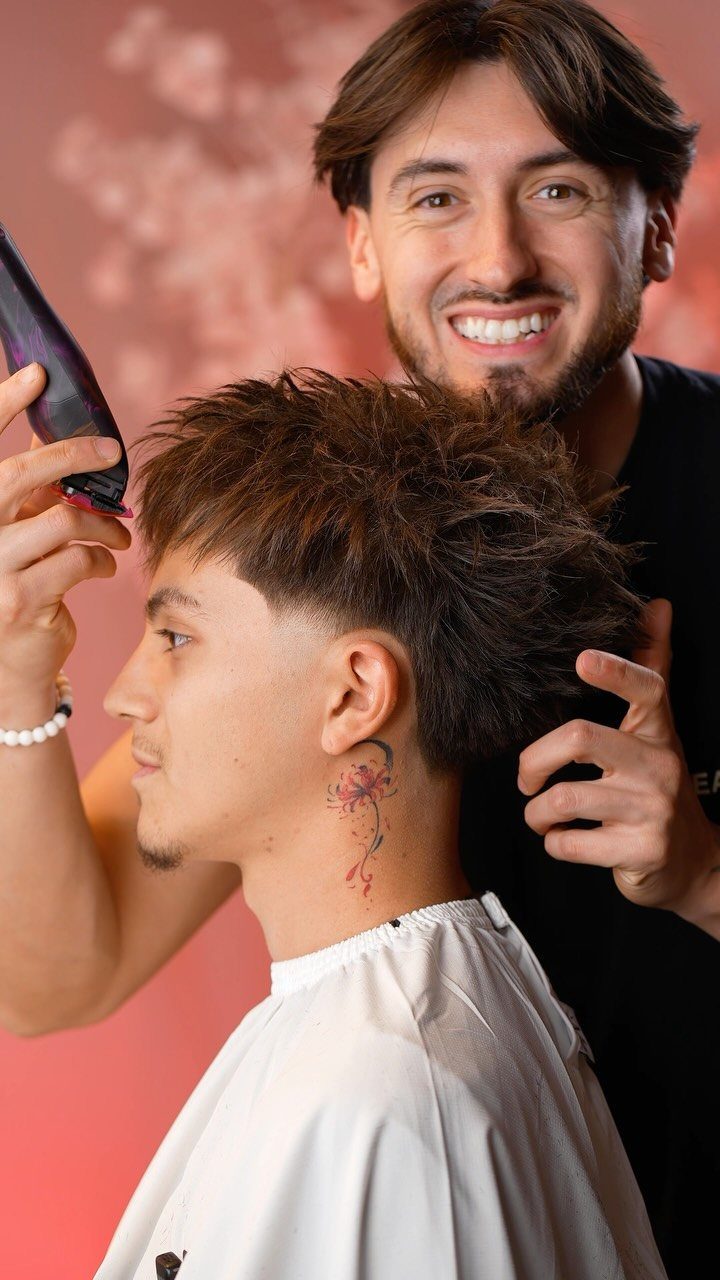 Man with spiky textured hair and neck tattoo being styled by a barber.