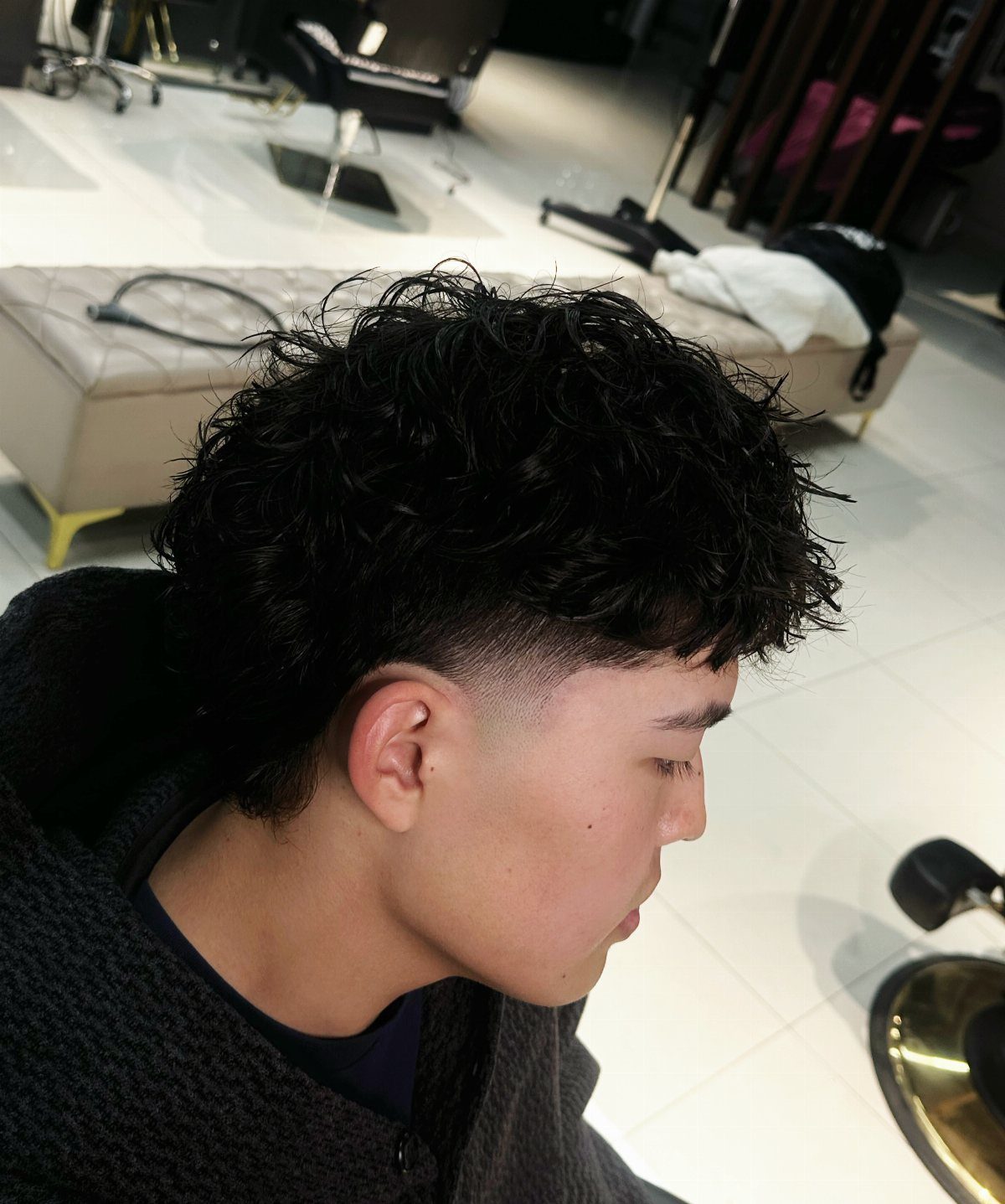 Young man with curly textured hair on top and a low taper fade haircut.
