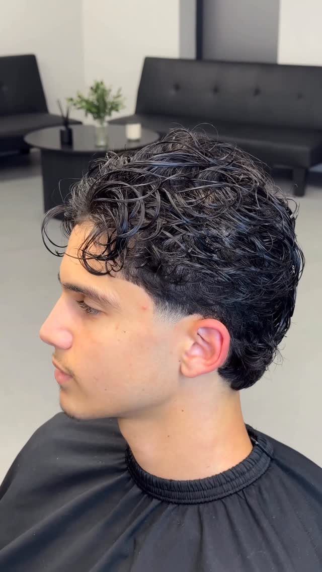 Young man with curly wet-look flow hair and a clean taper fade haircut.