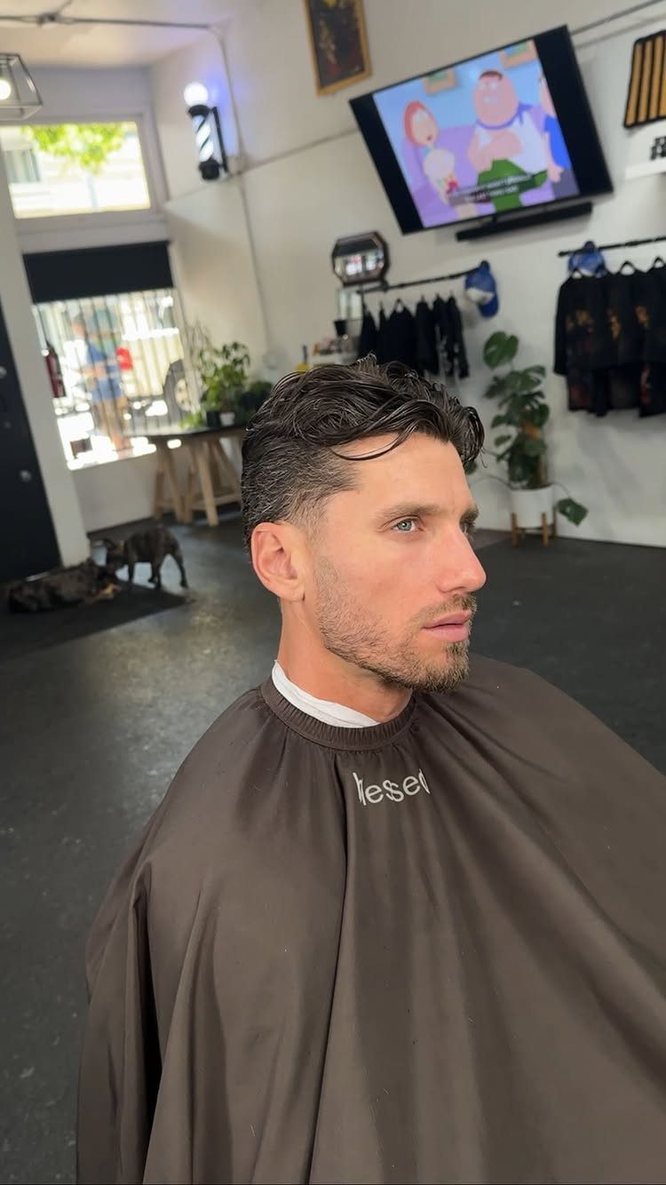 Man with dark hair brushed back and tapered sides in a barber shop