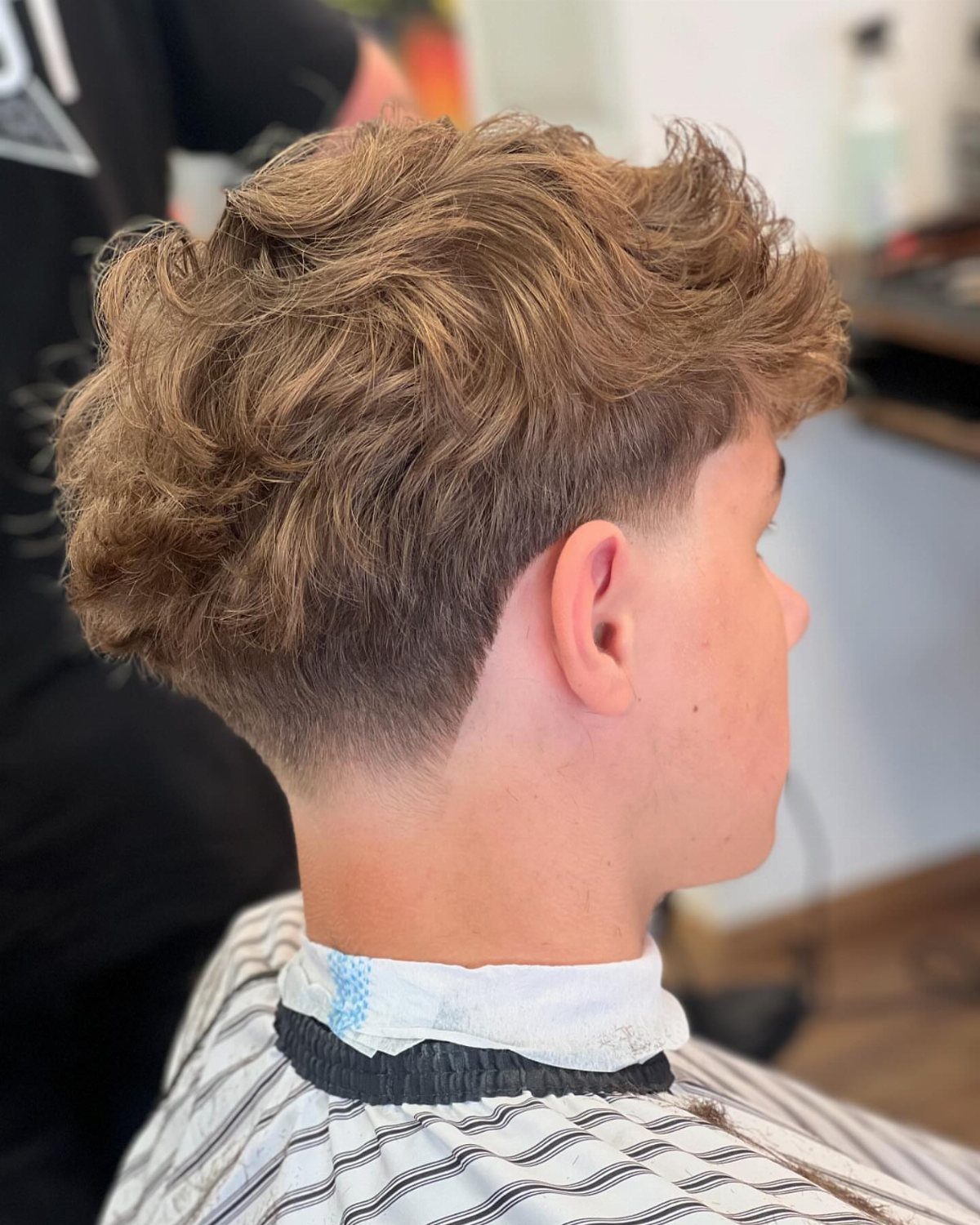 Young man with a brush up hairstyle and low taper fade in a barbershop.