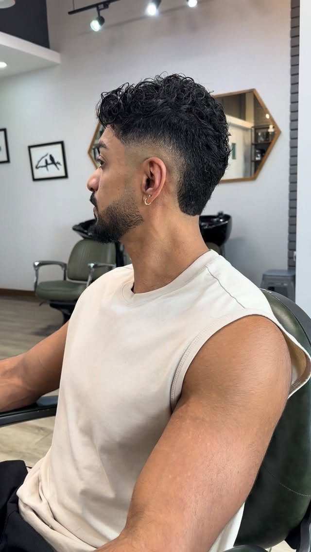 Man with curly hair and a classic low taper fade in a barbershop.