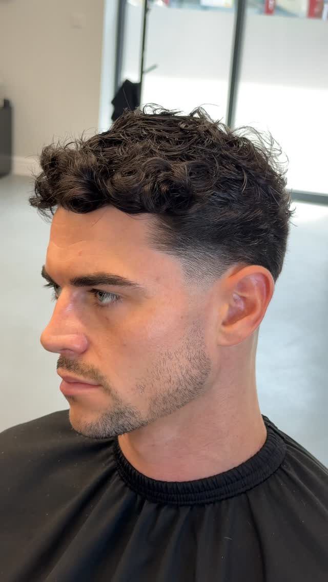 Man with dark curly hair on top and a clean low taper fade.