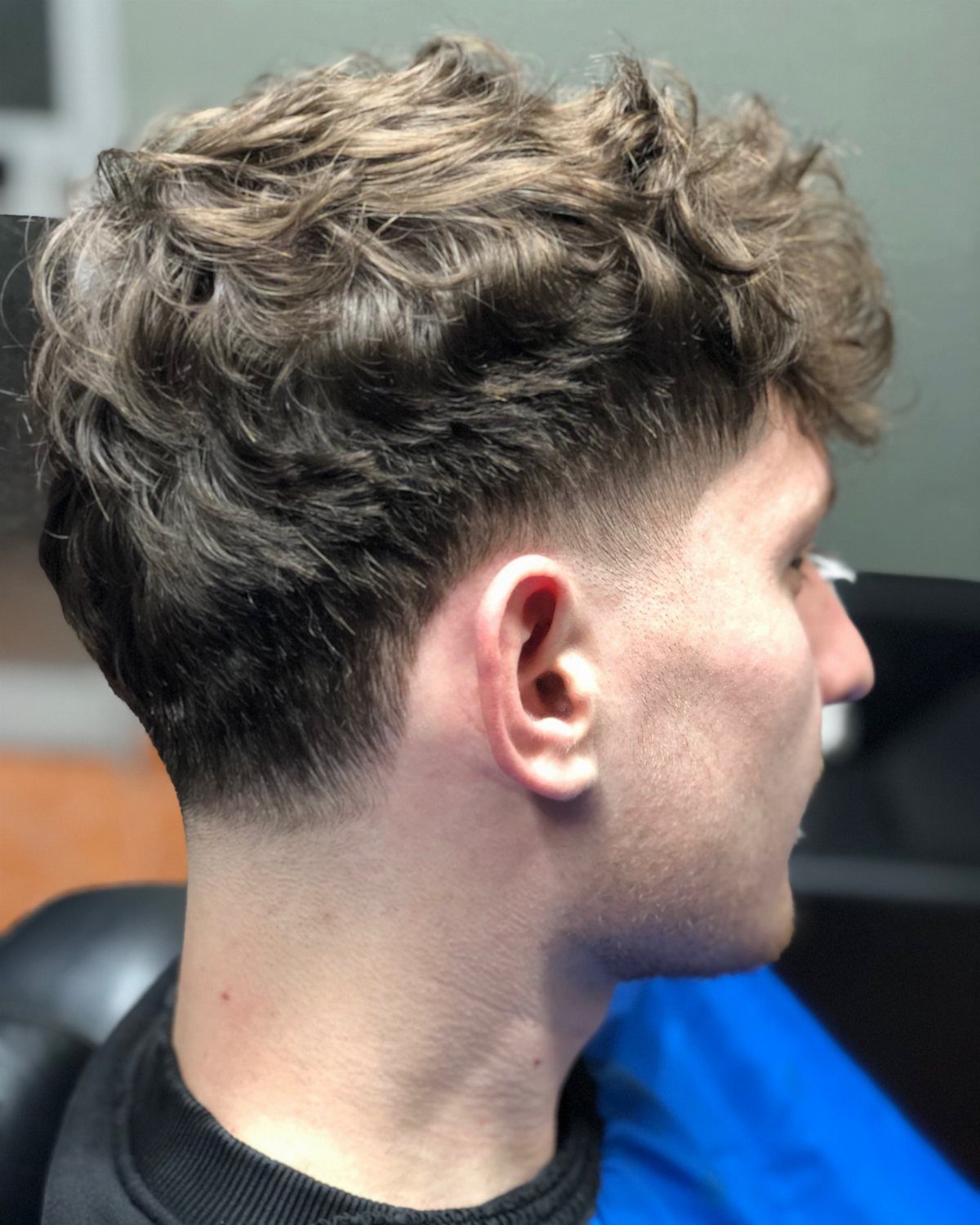 Man with voluminous wavy brown hair and a clean low taper fade haircut.