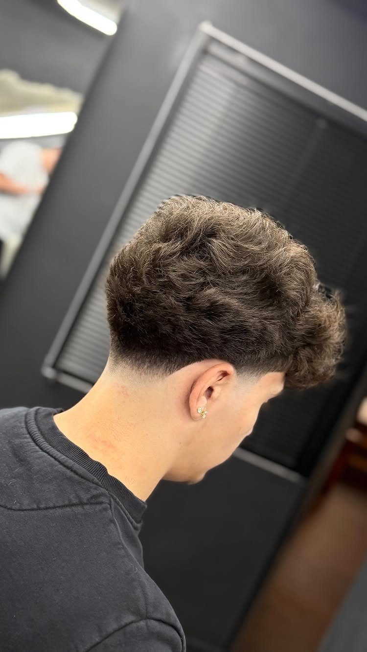 Man with shaggy brown wavy hair and a clean low taper fade haircut.