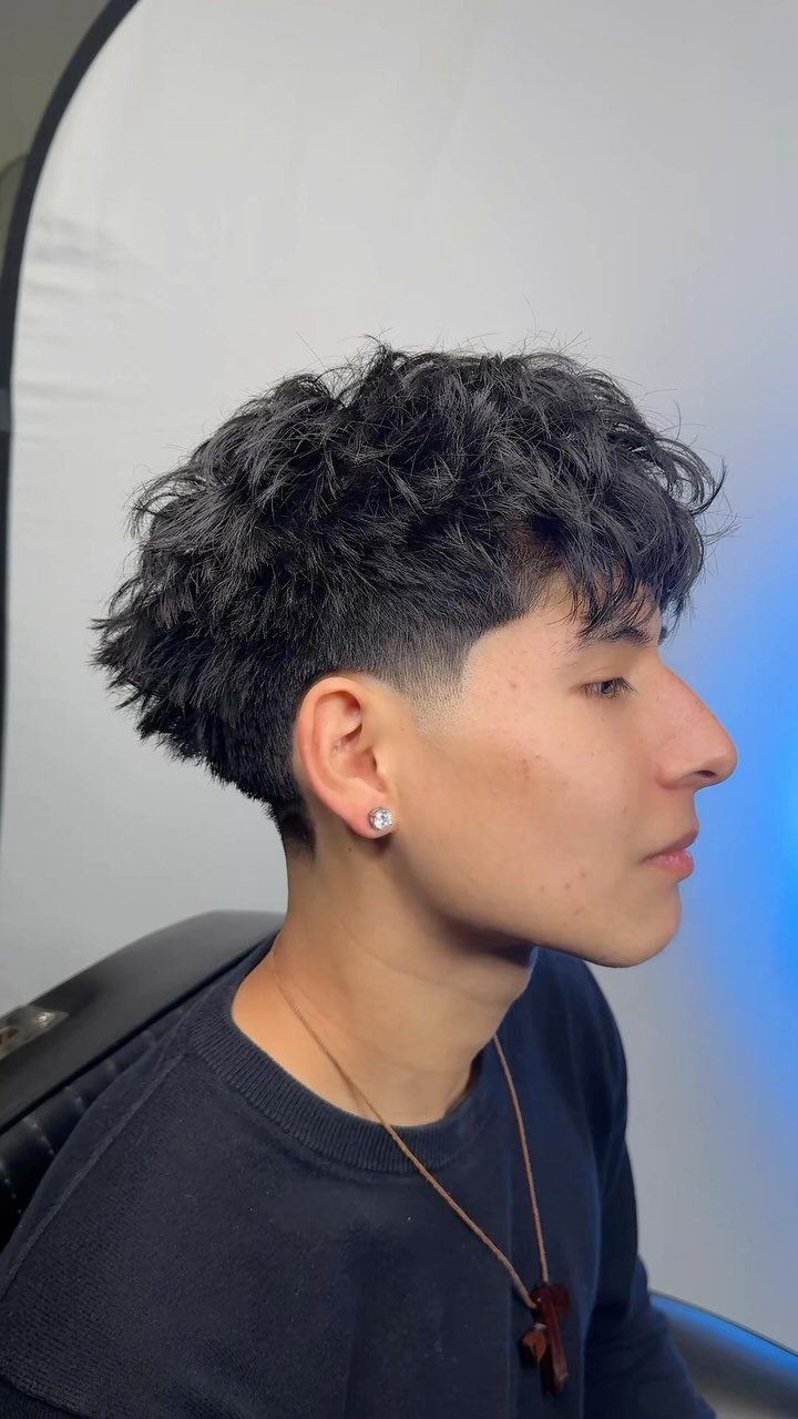 Young man with a low taper fade and messy curly hair on top.