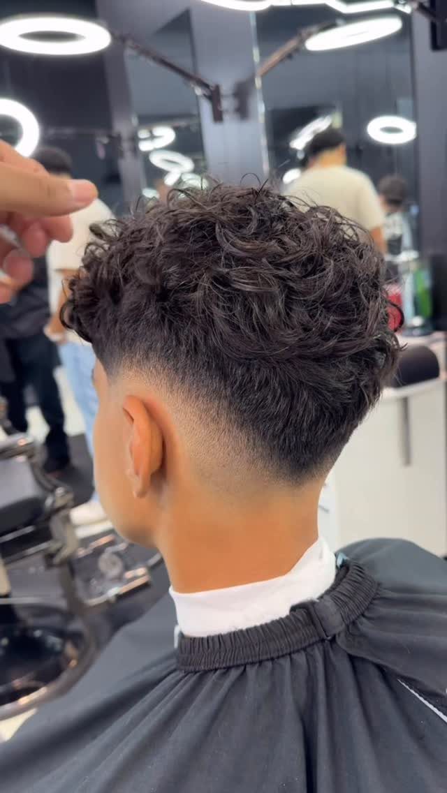 Person with dark curly hair on top and a clean low taper fade.