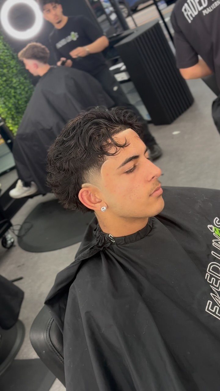 Young man with a low taper mullet haircut in a professional barbershop setting.