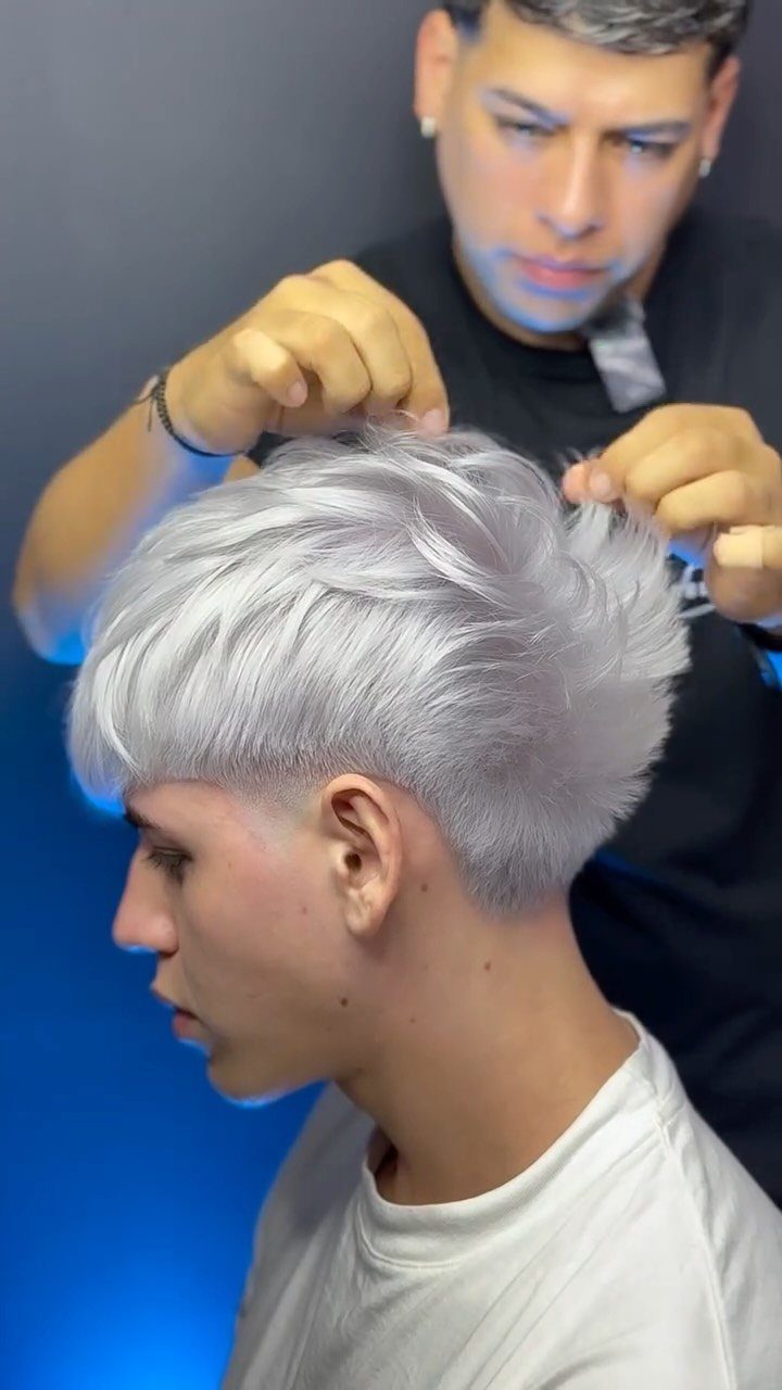 Man with silver-white hair and a low taper fade being styled by a barber.