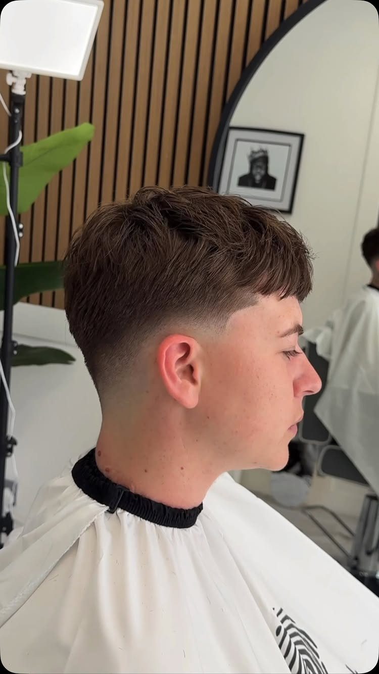 Young man with a low taper fade and straight brown hair in a barbershop.