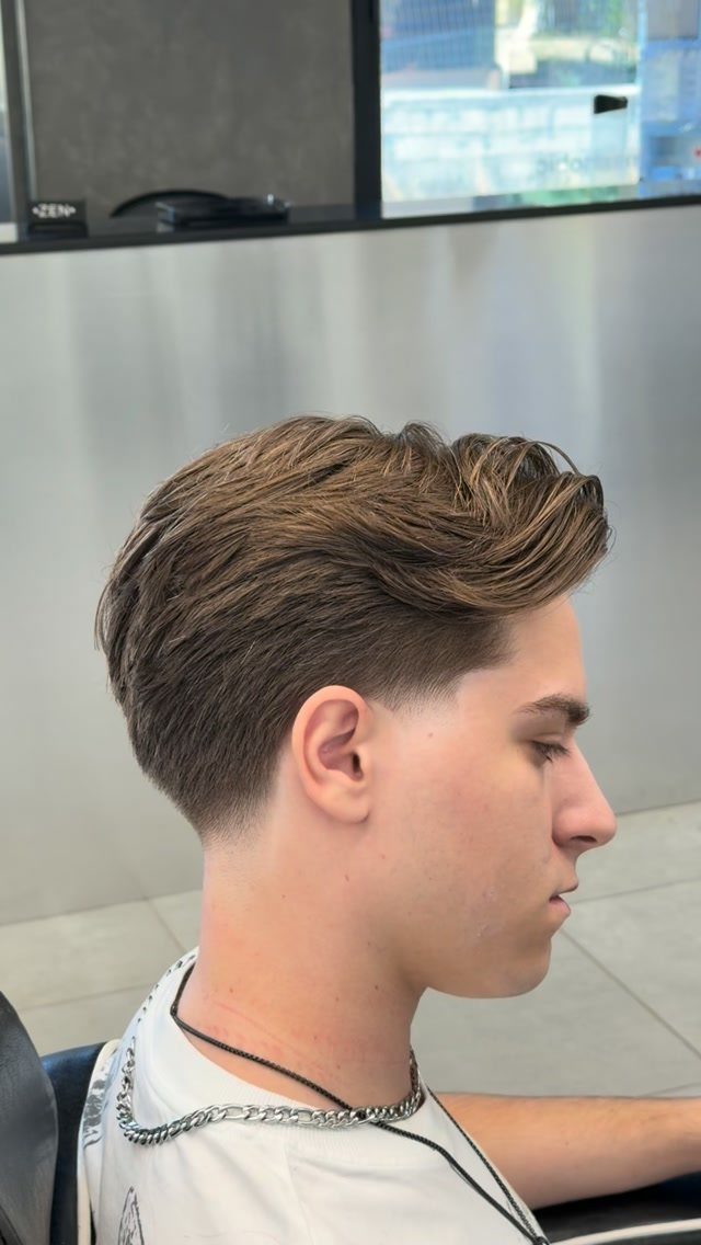 Young man with brown hair styled in a side part and low taper fade.