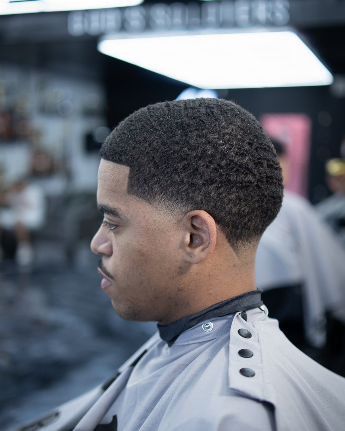 Man with a clean temple fade haircut wearing a grey barber cape.