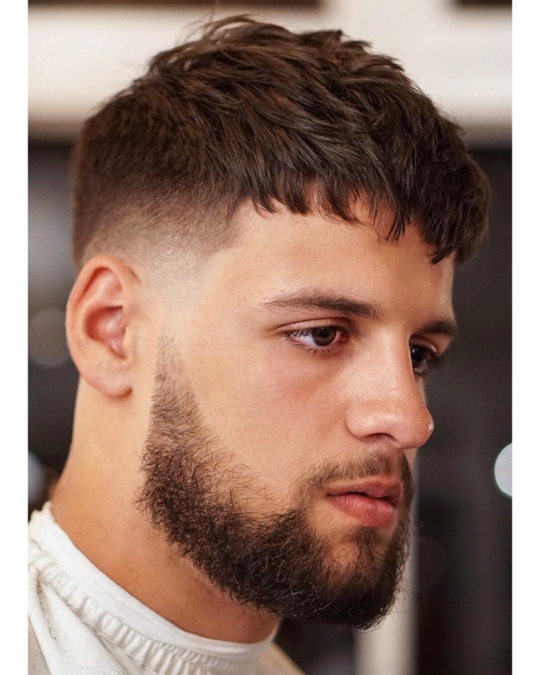 Man with a textured crop haircut and a groomed beard looking sideways.