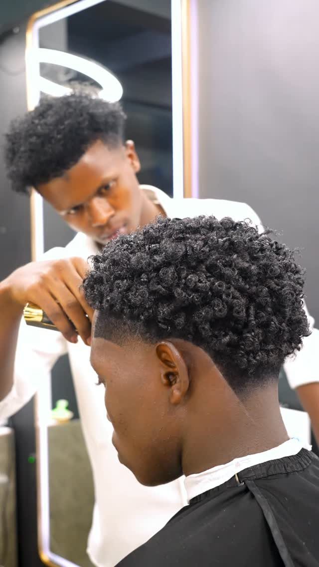 Man with voluminous mini curls getting a haircut from a barber in a shop.