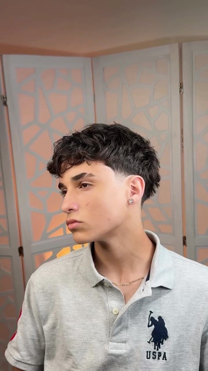 Young man with dark wavy hair and a low taper fade haircut.