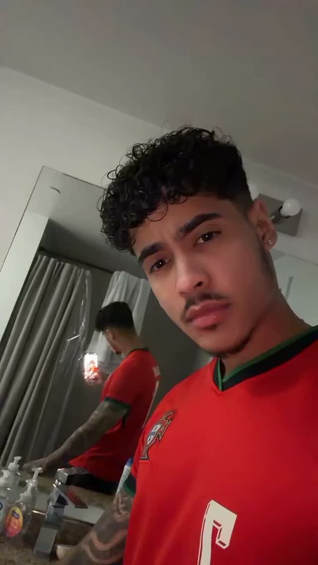 Young man with curly medium length hair and faded sides wearing red jersey