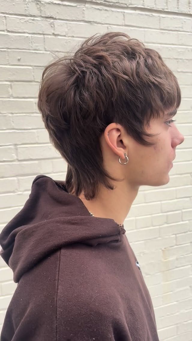 Young man with a brown edgy mullet haircut and a brown hoodie.