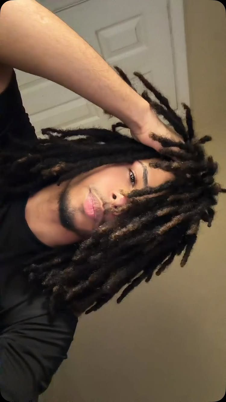 Man with long dark brown freeform dreadlocks posing in a black t-shirt.