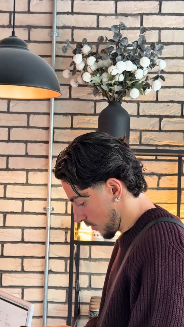 Man with dark medium flow haircut swept back, wearing a maroon ribbed sweater.
