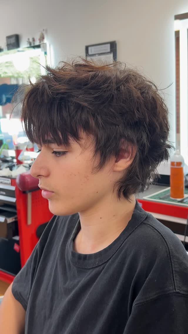 Young man with a brown layered shag haircut in a barbershop setting.