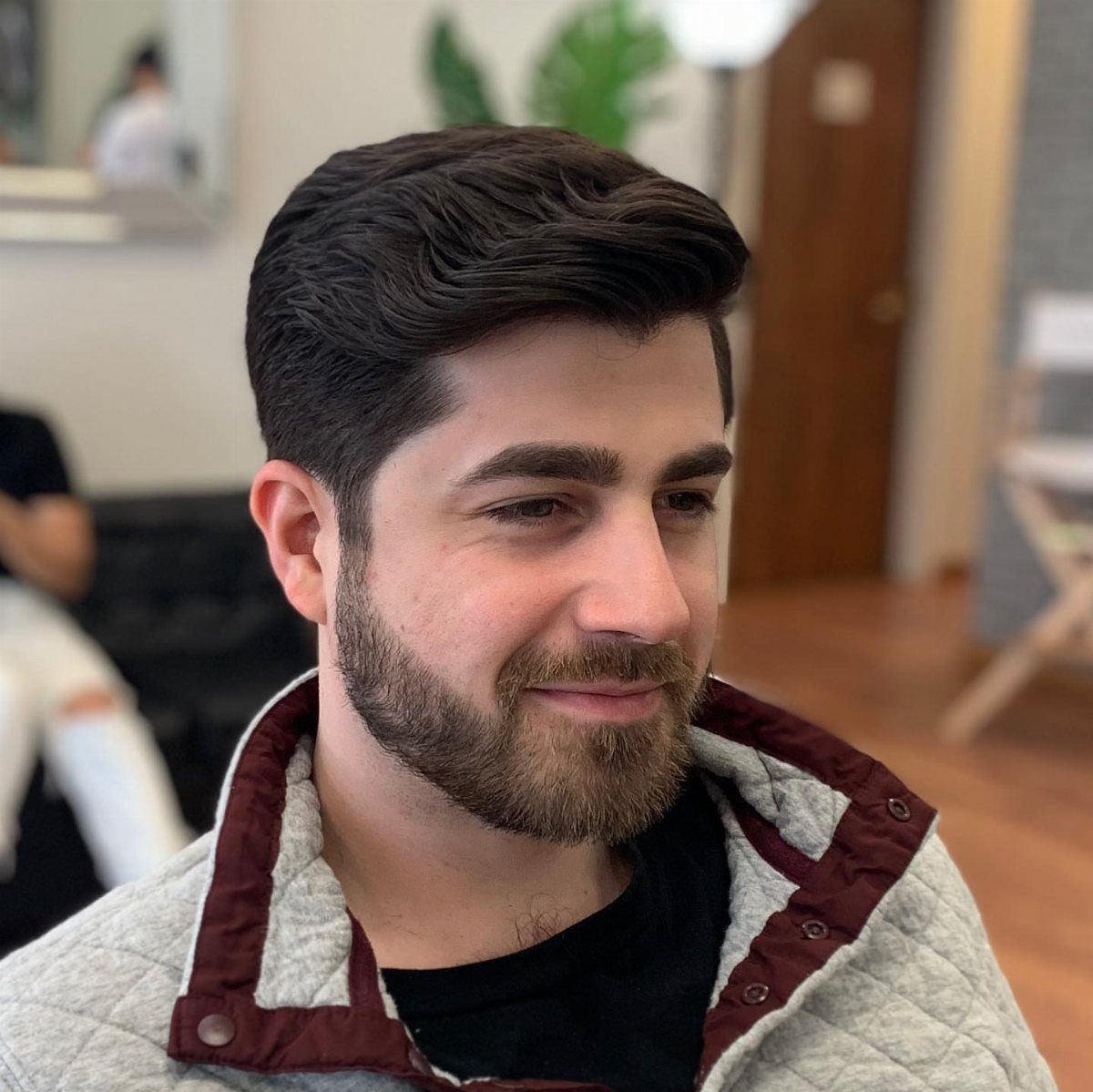 Man with dark brown hair styled in a side part and a groomed beard.