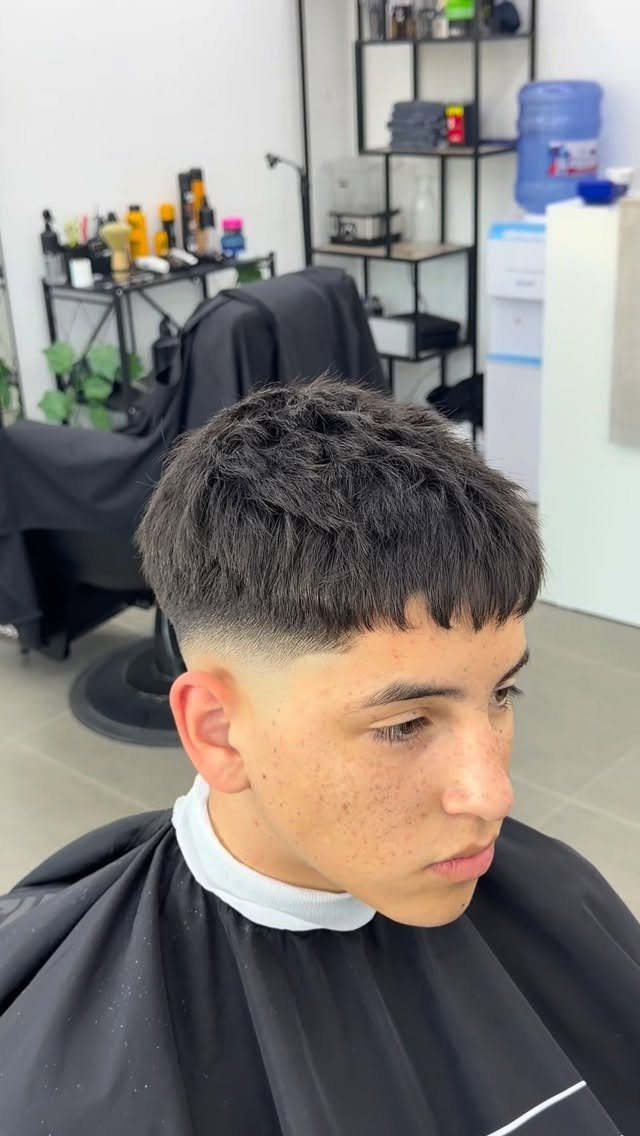 Young man with a textured French crop haircut and faded sides in a barbershop.