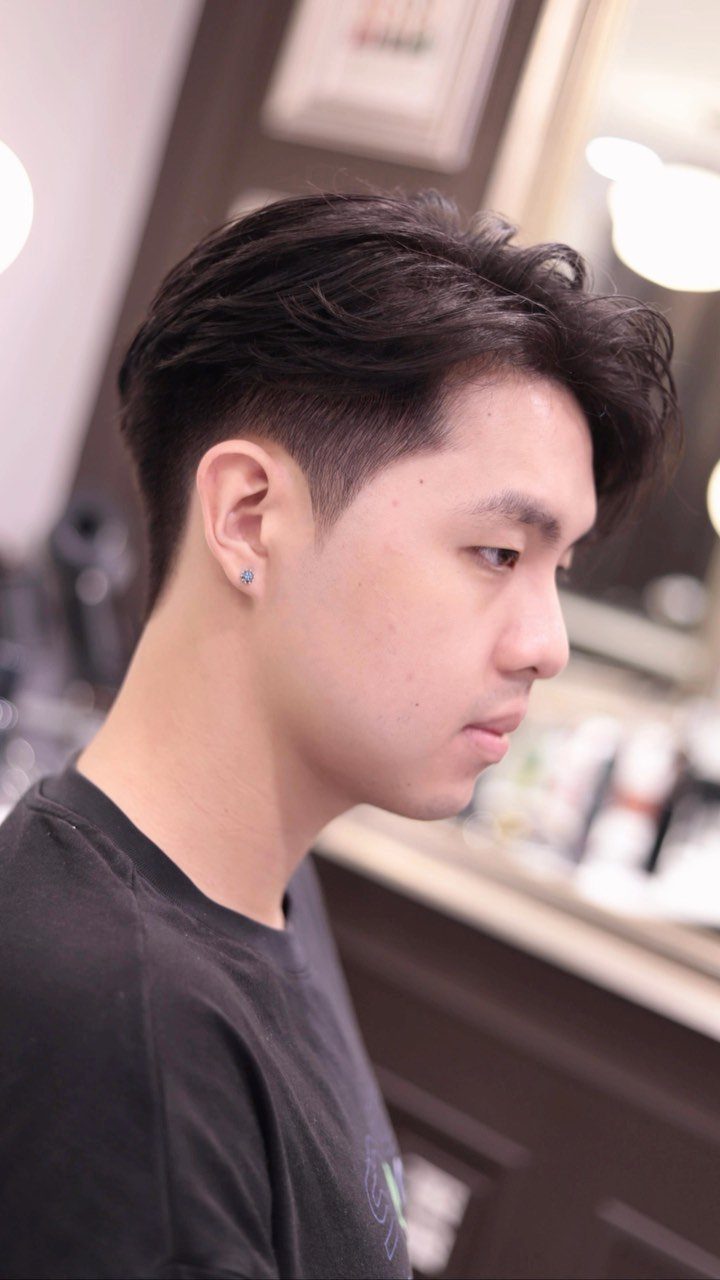 Man with a dark undercut haircut and styled top in a barbershop setting.