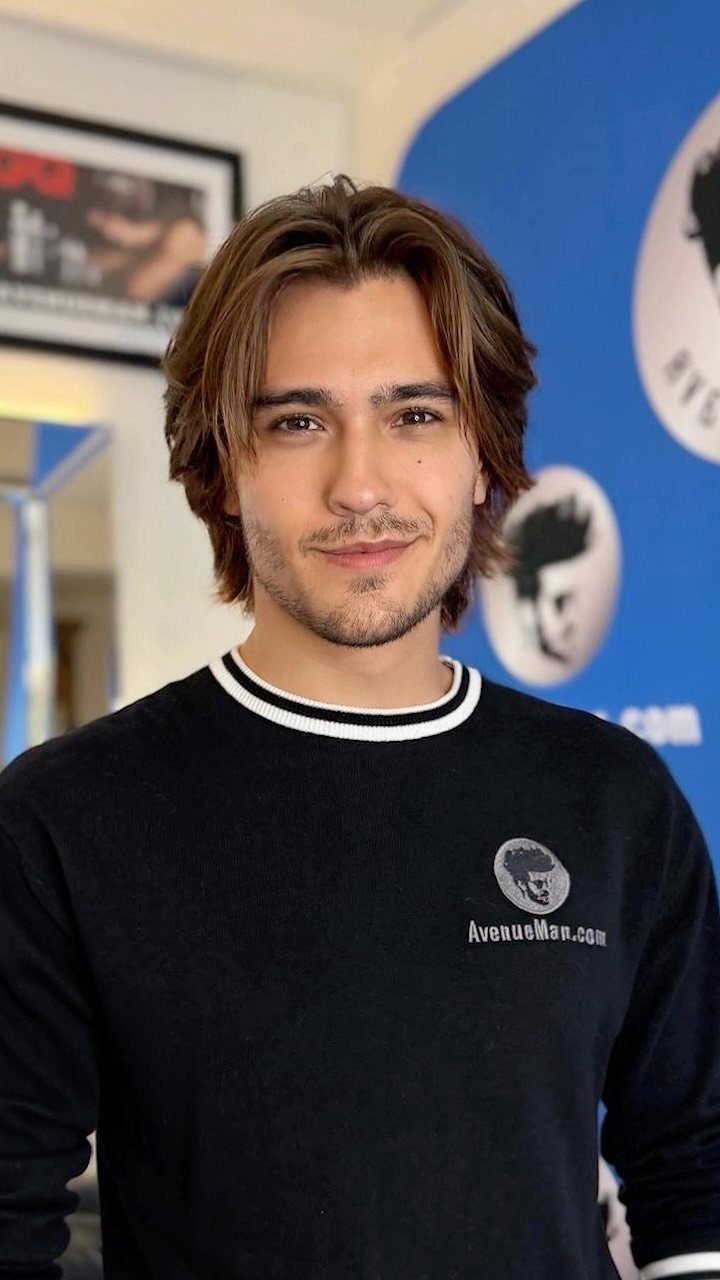 Man with medium-length brown wavy hair styled in a wings haircut and light beard.