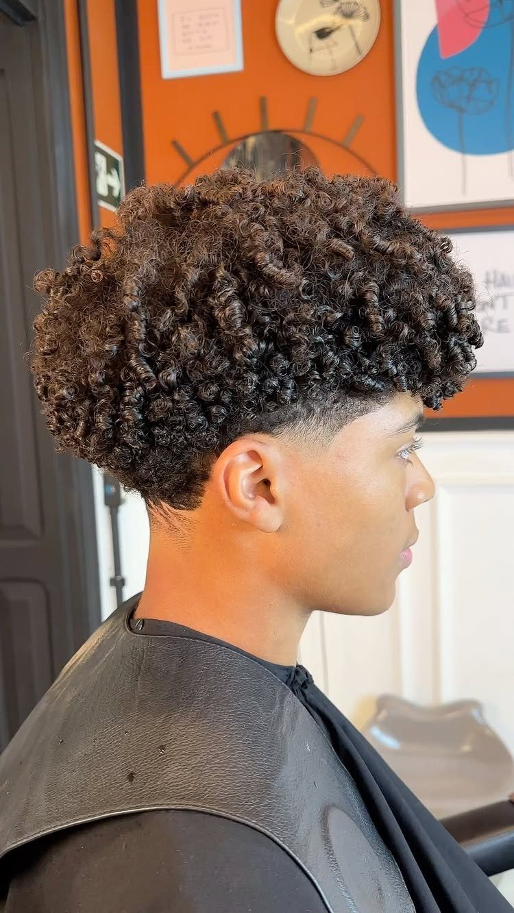 Young man with tightly coiled hair on top and faded sides in a barbershop.
