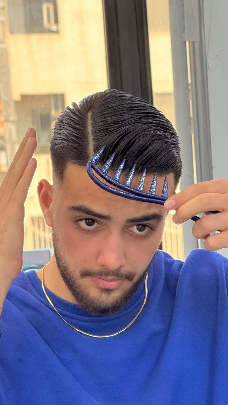 Man with dark hair styled in a comb over using a blue comb.