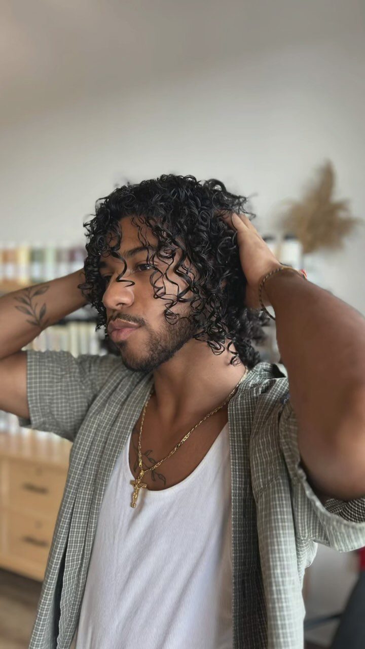 Man with medium-length dark curly hair wearing a white t-shirt and checkered shirt.