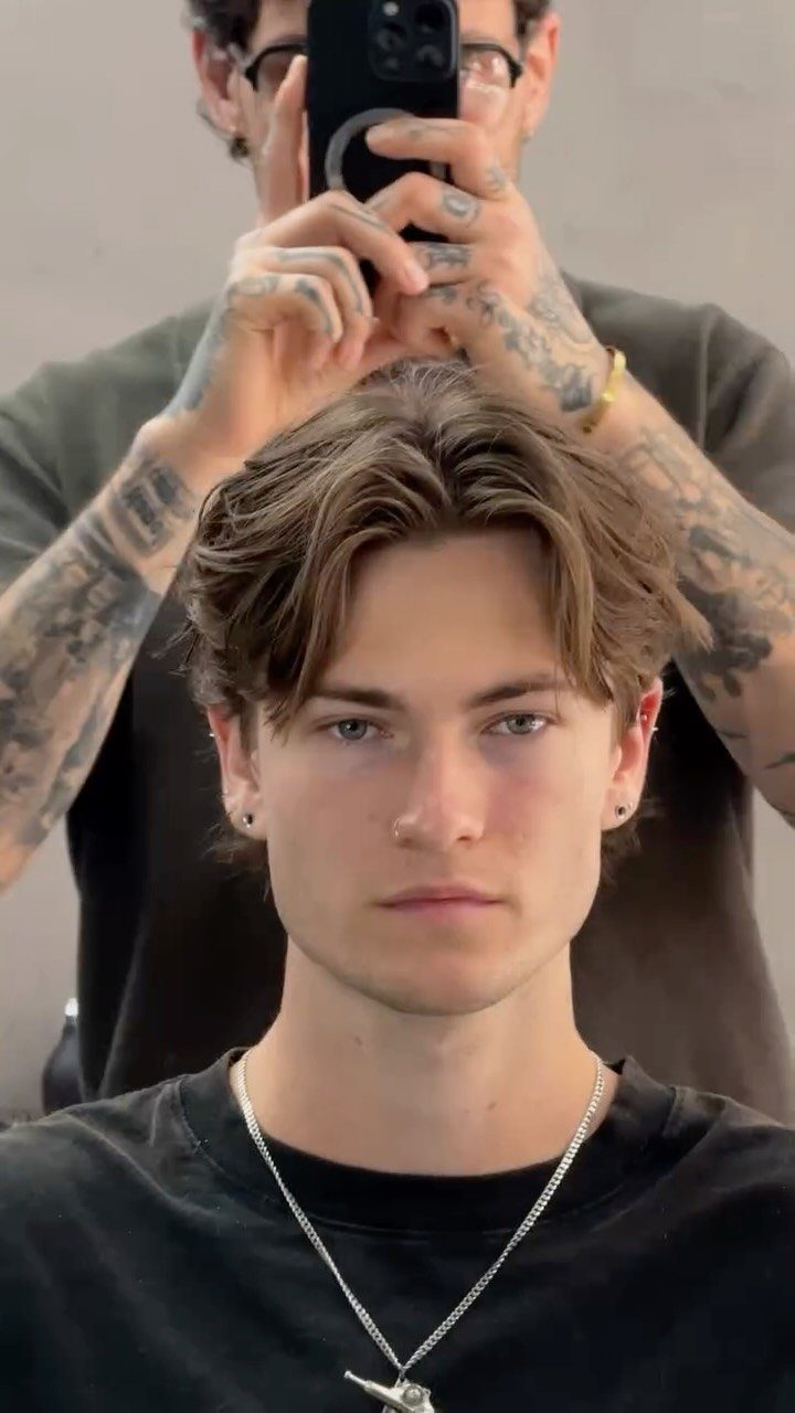 Young man with light brown hair styled in a middle part curtain haircut.