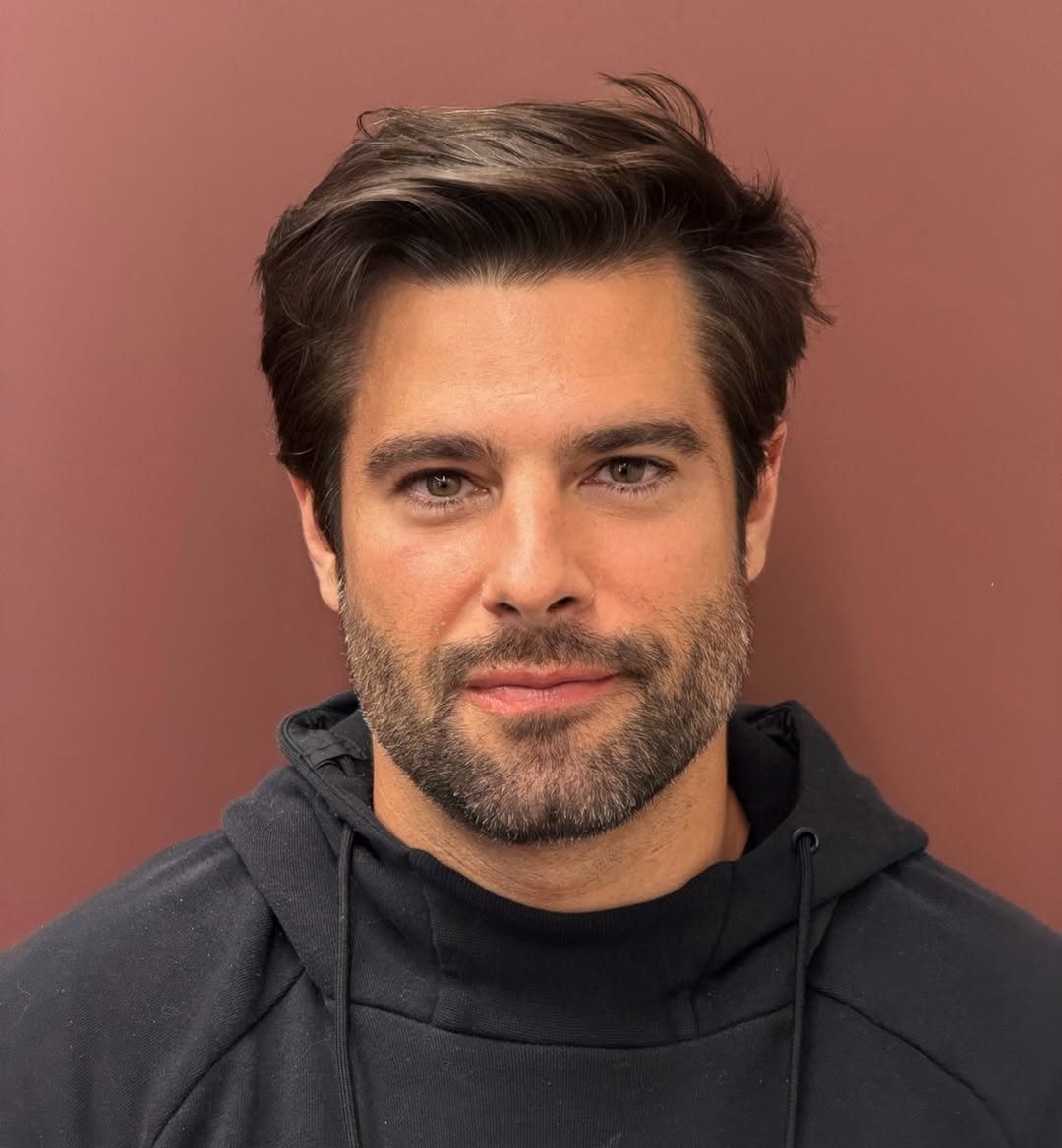 Man with medium-length brown hair swept back in a flow style and groomed beard.