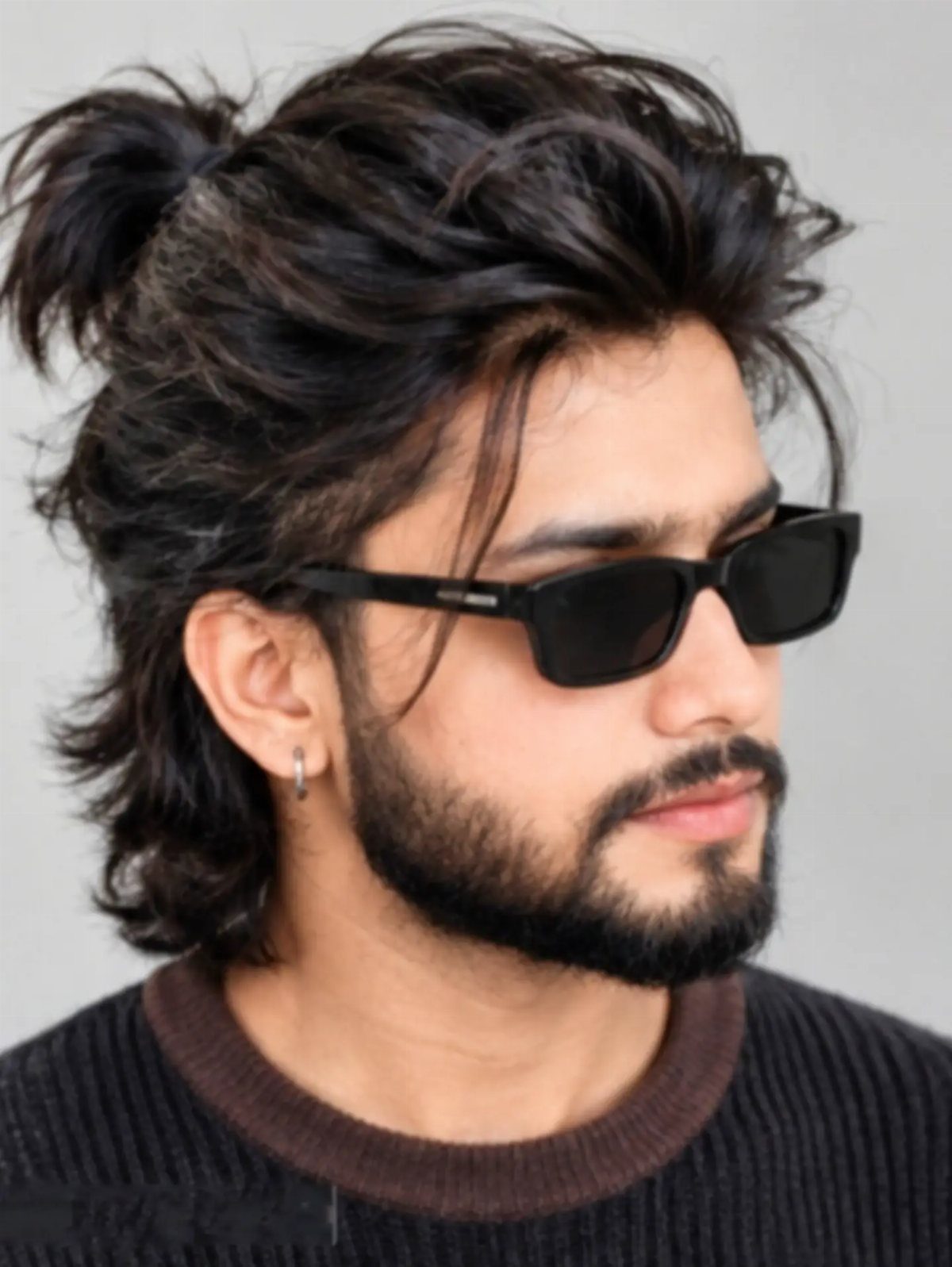 Man with dark wavy hair styled in a half-up bun wearing black sunglasses.