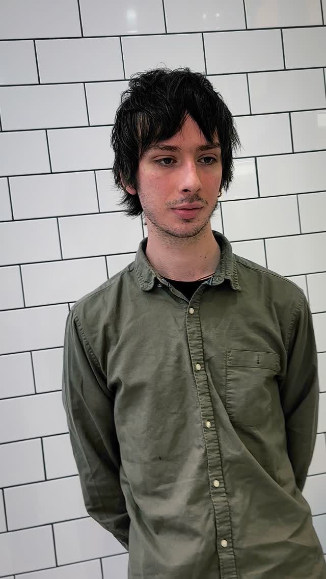 Man with dark medium-length hair and a messy fringe against white tiles.