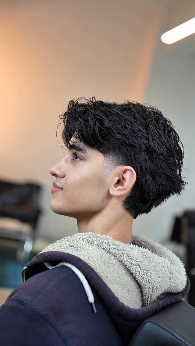 Young man with a dark modern mullet haircut and a fleece-lined hoodie.