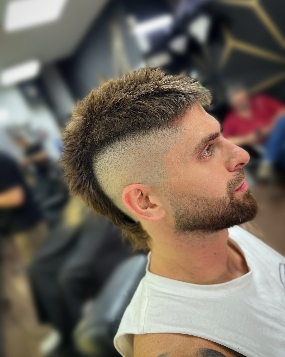 Man with a brown mohawk haircut and groomed beard in a barbershop.