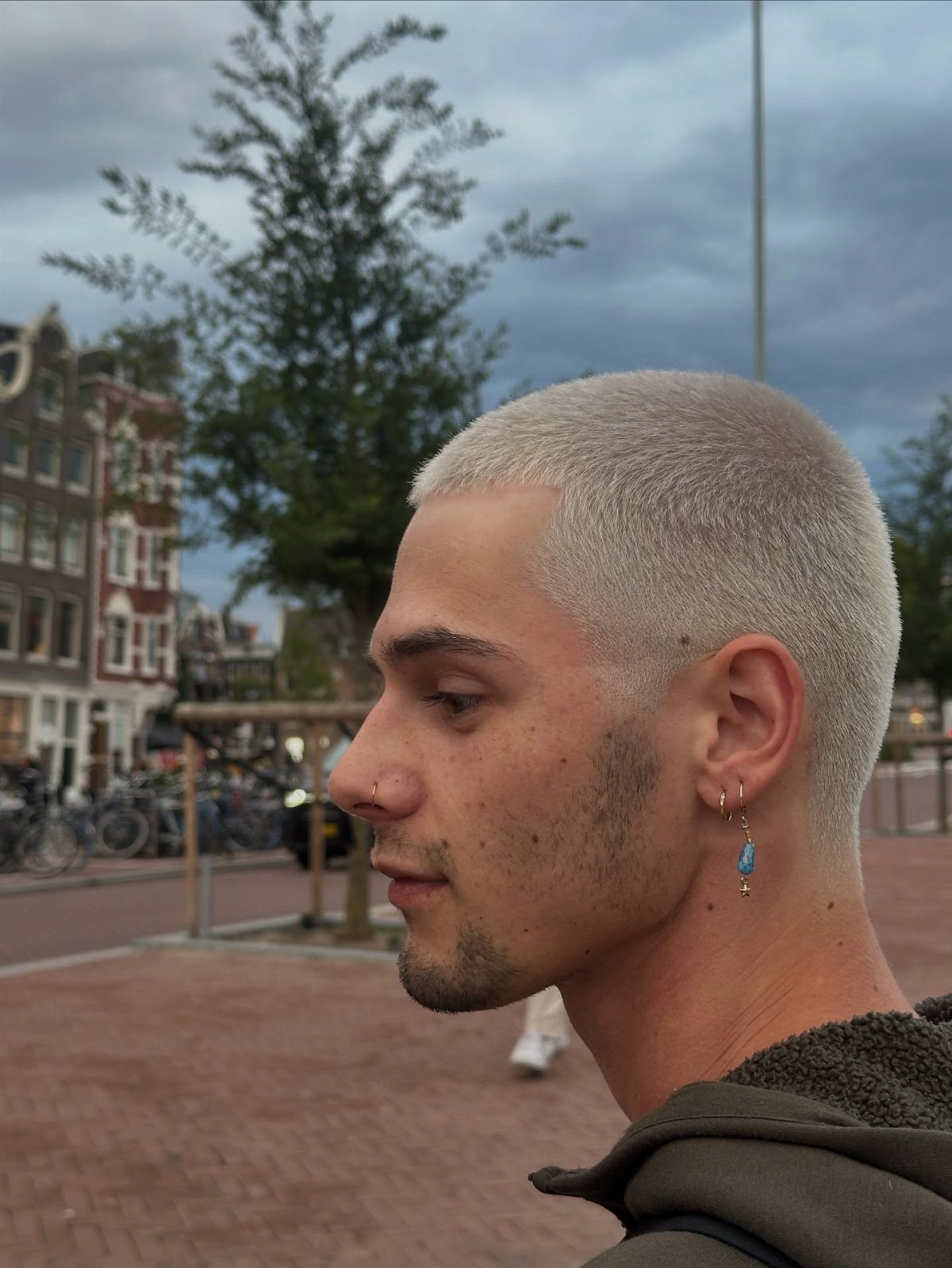 Man with a short bleached blonde buzz cut in a city setting.
