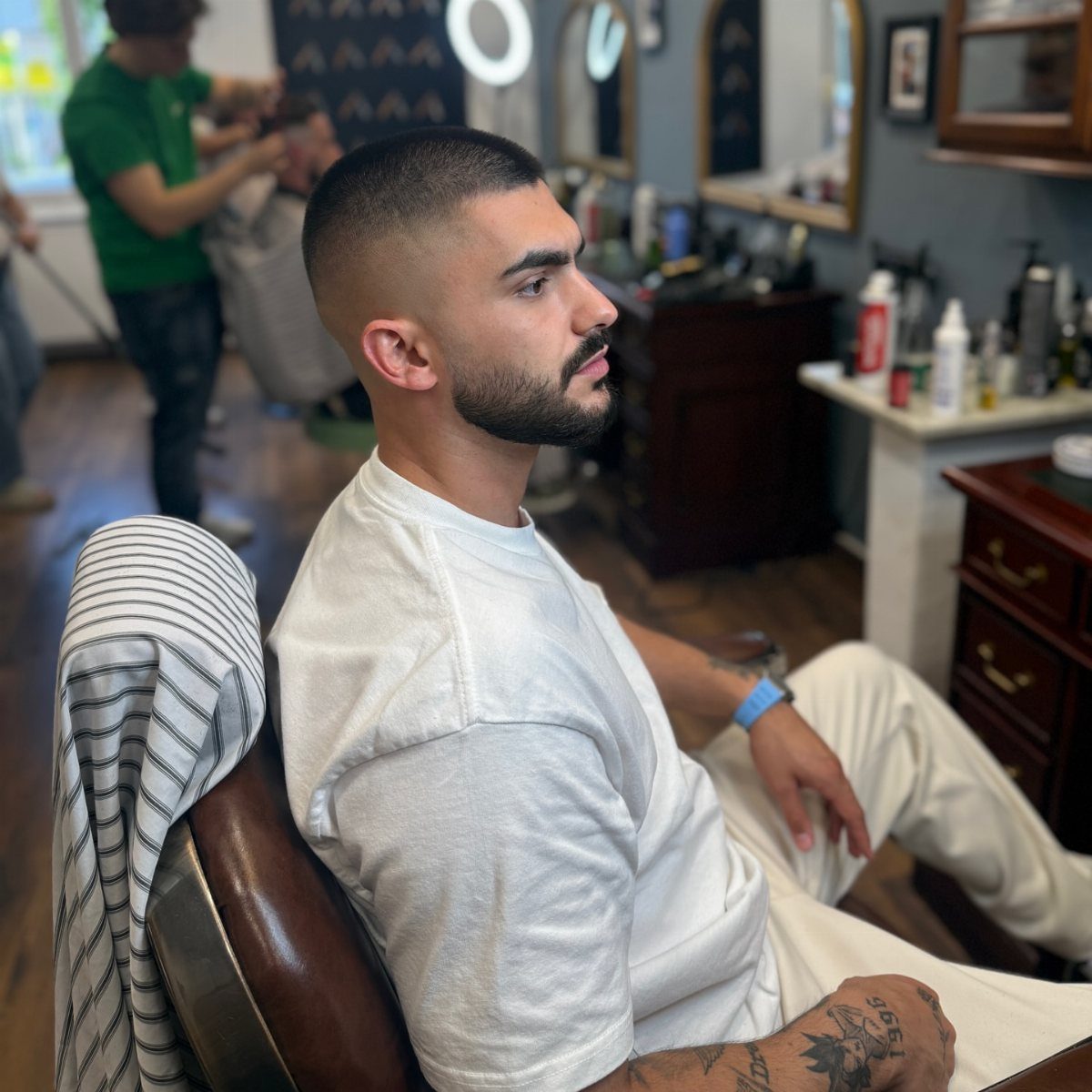 Man with a buzz cut and drop fade sitting in a barber chair.