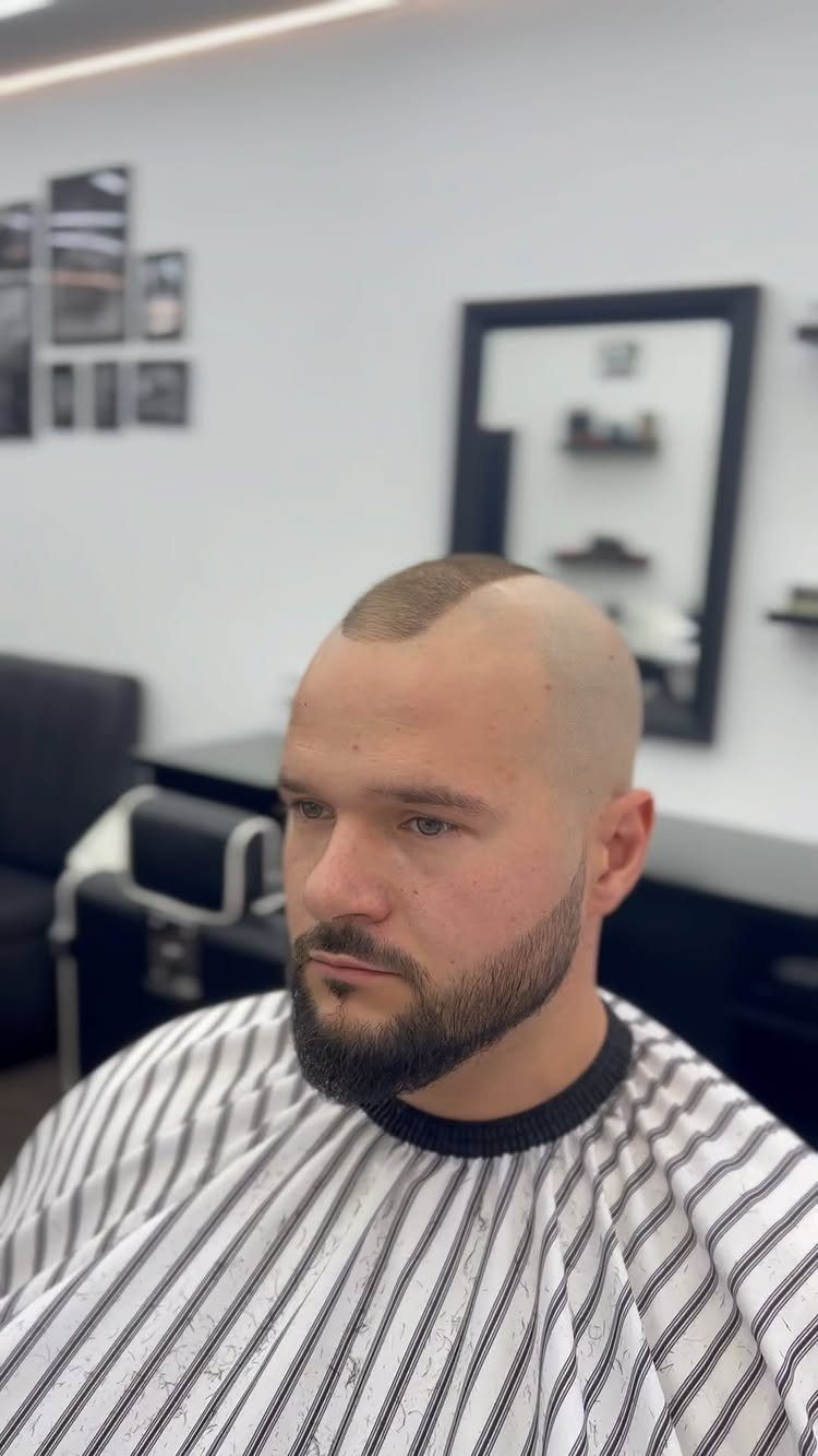 Man with a mohawk buzz cut and groomed beard wearing a barber cape.
