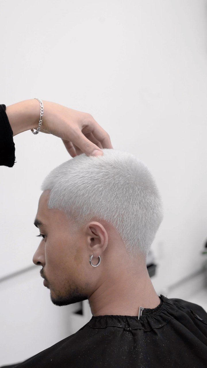 Man with a silver buzz cut hairstyle wearing a black barber cape.