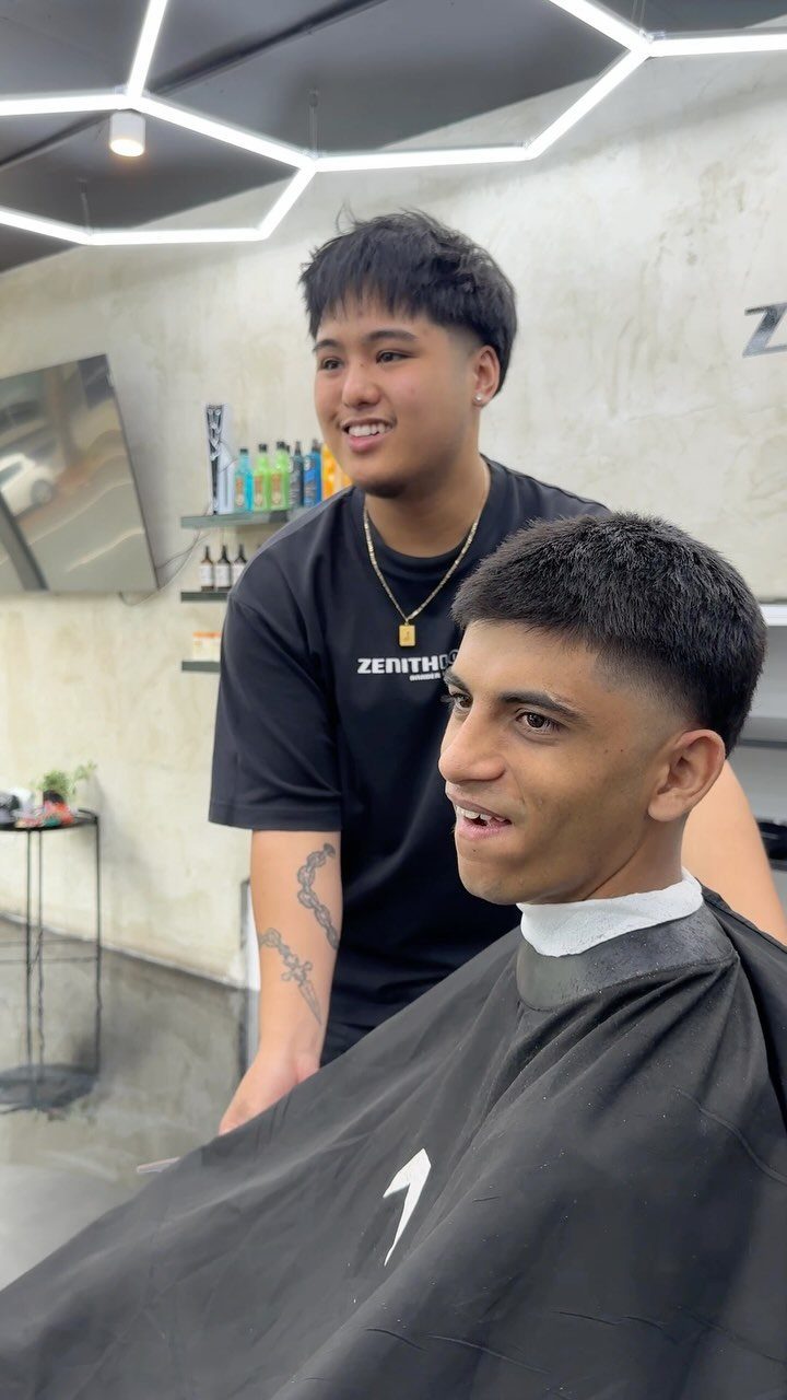 Man with a tapered buzz cut sitting in a barber chair at a shop.