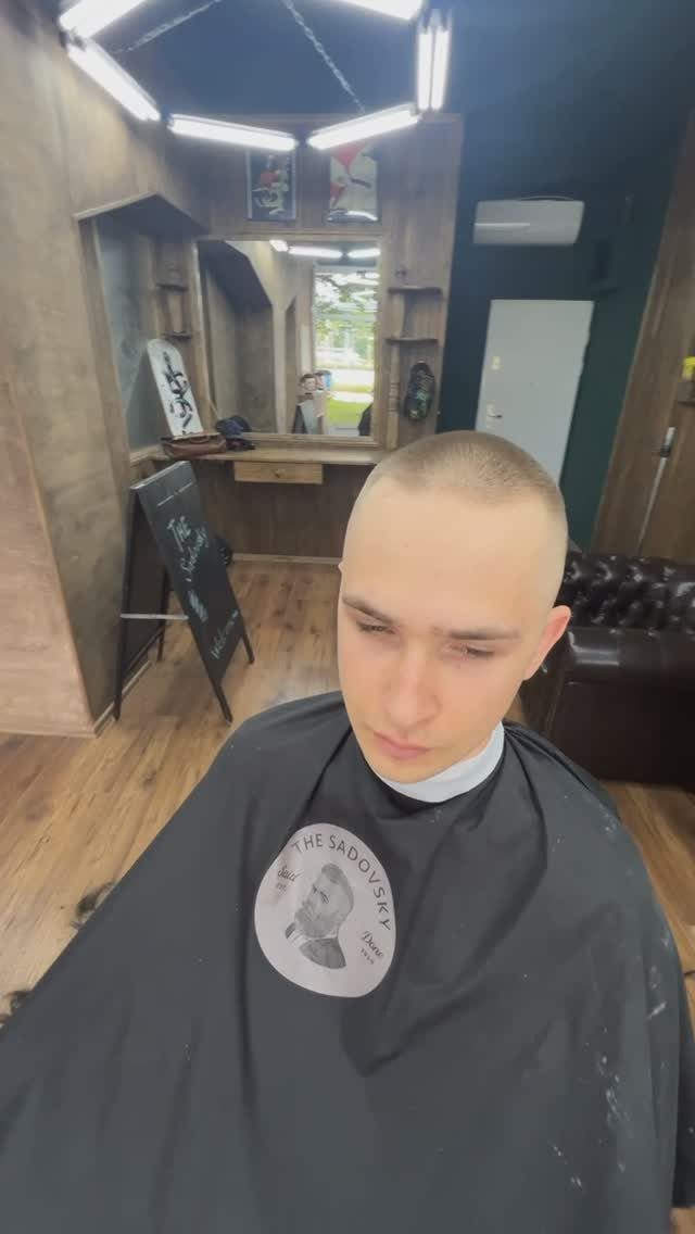 Man with a uniform short buzz cut wearing a black barber cape.